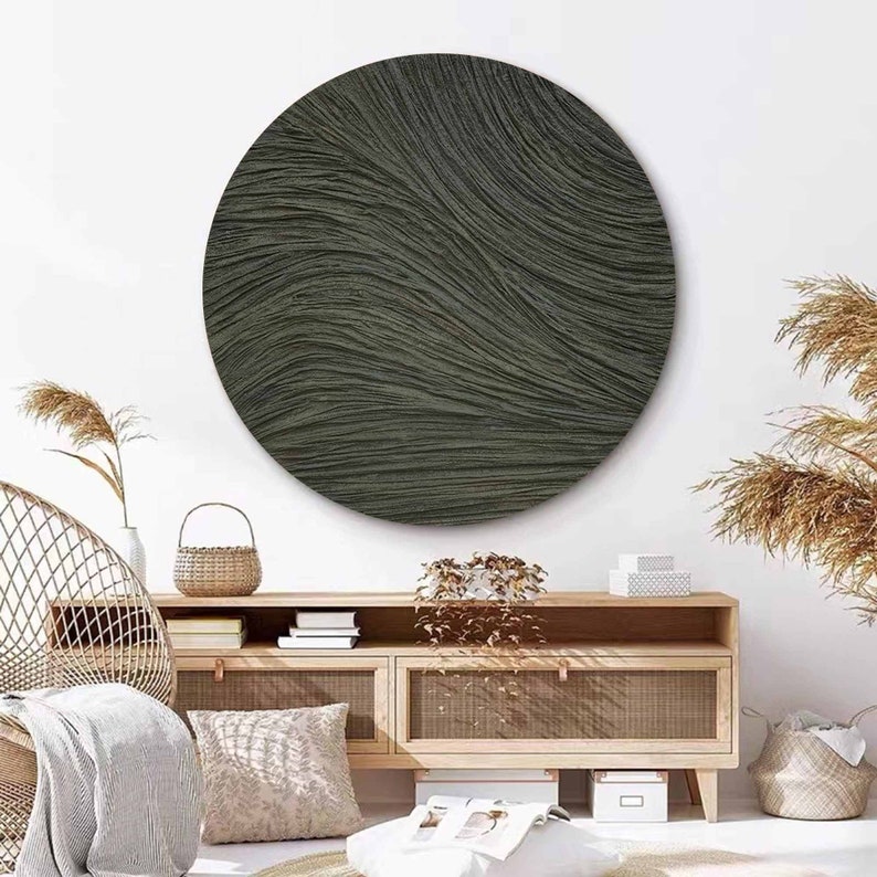 May include: A large, round wall art piece with a textured, wave-like pattern in shades of dark green. The artwork is mounted on a white wall above a wooden cabinet with woven accents, creating a modern, minimalist aesthetic.