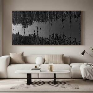 Puede incluir: Una pintura abstracta en blanco y negro cuelga sobre un sof&aacute; seccional blanco con almohadas beige. El sof&aacute; est&aacute; en una sala de estar con una mesa de caf&eacute; blanca y una alfombra en blanco y negro.