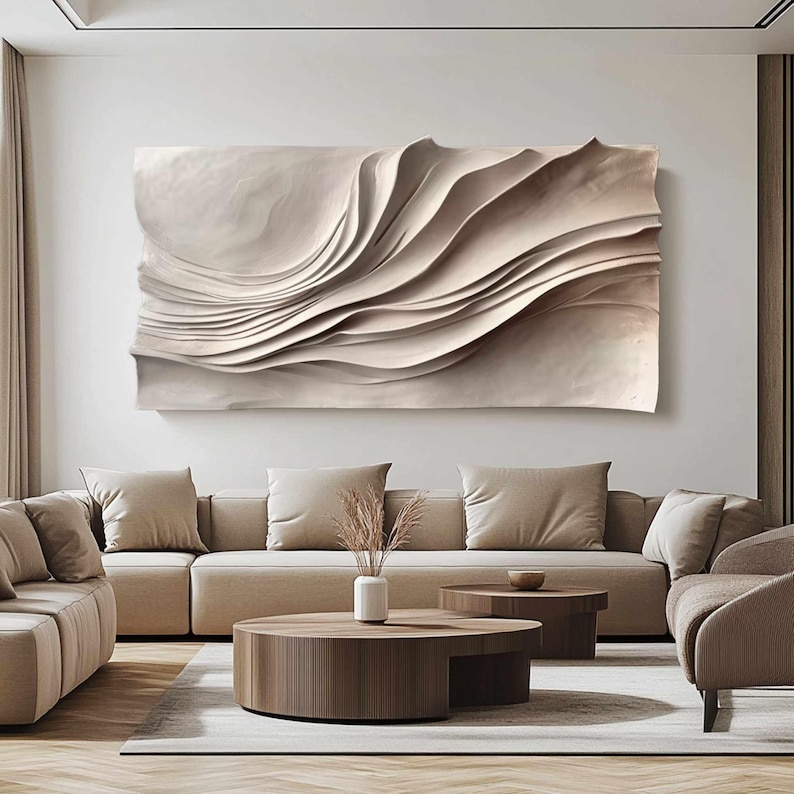 May include: A large, abstract wall art piece with a layered, wave-like design in neutral beige tones. The artwork hangs above a beige sectional sofa, complementing the room's modern, minimalist aesthetic. The room also features two round coffee tables and a vase with dried plants.
