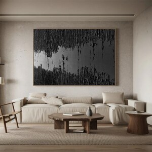 Puede incluir: Un sal&oacute;n moderno con una gran pintura abstracta en tonos negros y grises colgada en la pared sobre un sof&aacute; seccional beige. El sof&aacute; tiene una mesa de centro de madera delante con un jarr&oacute;n y un libro encima. Hay una mesa auxiliar de madera con un jarr&oacute;n encima a la derecha del sof&aacute;.