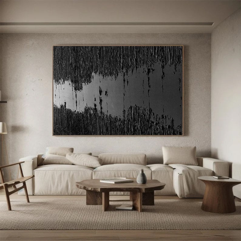 Puede incluir: Un sal&oacute;n moderno con una gran pintura abstracta en tonos negros y grises colgada en la pared sobre un sof&aacute; seccional beige. El sof&aacute; tiene una mesa de centro de madera delante con un jarr&oacute;n y un libro encima. Hay una mesa auxiliar de madera con un jarr&oacute;n encima a la derecha del sof&aacute;.