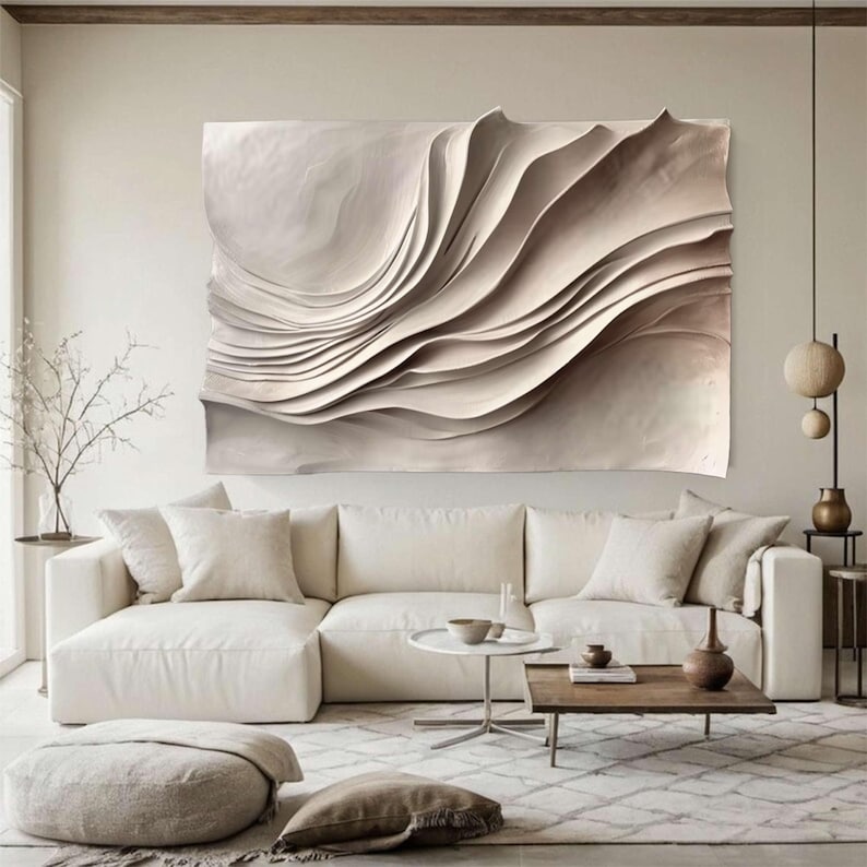 May include: Large, abstract wall art featuring a layered, wave-like design in neutral tones. The artwork is mounted above a white sectional sofa in a modern living room setting. The piece adds a touch of texture and visual interest to the space.