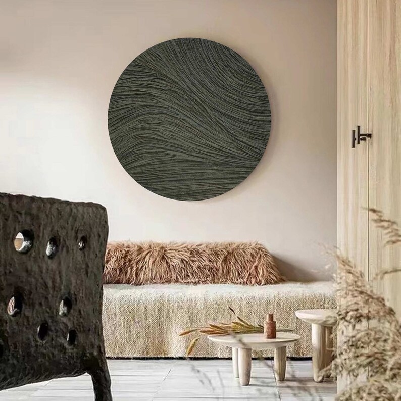 May include: A large, round, dark gray wall art piece with a textured, wave-like pattern. The artwork is mounted on a light-colored wall, creating a contrast. The room has a neutral color palette with natural textures.
