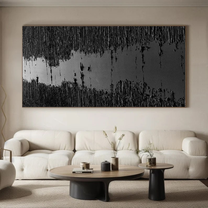 Puede incluir: Una pintura abstracta en blanco y negro con una superficie texturizada cuelga sobre un sof&aacute; blanco y una mesa de caf&eacute; de madera. La pintura tiene una orientaci&oacute;n horizontal y una franja gris en el medio.
