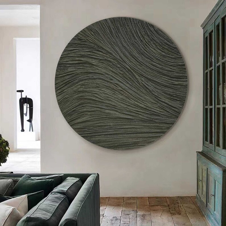 May include: A large, round, textured wall art piece in shades of gray and charcoal. The artwork features a flowing, wave-like pattern, creating a sense of movement and depth. The piece is mounted on a white wall, complementing the neutral tones of the art.