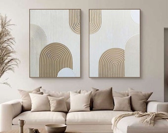 May include: Two abstract paintings with a white background and brown geometric shapes. The paintings are hung on a white wall above a beige couch.