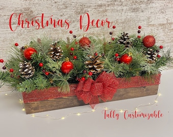 Puede incluir: Una caja de madera llena de vegetación, bayas rojas, piñas y adornos rojos. Un lazo rojo está atado alrededor de la caja. El texto "Christmas Decor" está escrito encima de la caja y "Fully Customizable" está escrito debajo de la caja.