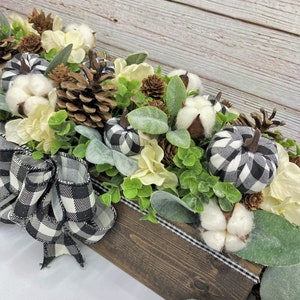 Pu&ograve; includere: Un centrotavola in legno decorato con boccioli di cotone bianco, pigne e zucche in tessuto a scacchi neri e bianchi. La scatola &egrave; decorata con un nastro a scacchi neri e bianchi.
