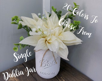 May include: A single white dahlia flower arrangement in a white Ball mason jar. The jar has a twine bow and the text "Ball Mason" is visible on the jar. The text "20 Colors To Choose From" and "Single Dahlia Jar" are written in white on a gray background.