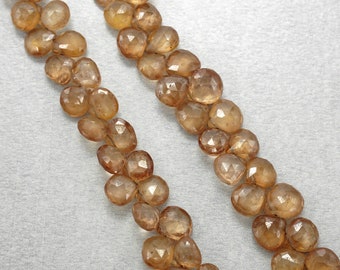 May include: Two strands of faceted, light amber-coloured gemstones. The stones have a rounded, irregular shape and are strung together. The background is a light grey fabric. The gemstones appear to be semi-precious.