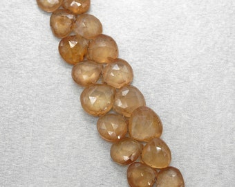 May include: A strand of faceted, heart-shaped, amber-coloured gemstones. The gems are translucent, catching the light and displaying multiple facets. The beads are strung together, ready for jewellery making.
