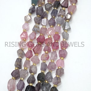 May include: Strands of faceted gemstone beads in shades of pink, purple, gray, and green. The beads are strung with gold-colored spacers. The text "RISING GEMS AND JEWELS" is visible in the image.