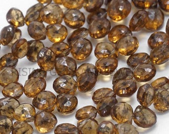 May include: A scattering of amber-coloured, faceted gemstones. The gemstones are rounded with multiple facets that reflect light, creating a sparkling effect. The colour ranges from light to dark amber.