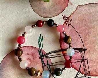 May include: A beaded bracelet featuring a variety of colorful gemstones, including pink, red, brown, and blue beads. The bracelet is strung on an elastic cord and accented with gold-colored spacers. The bracelet is displayed on a watercolor background.