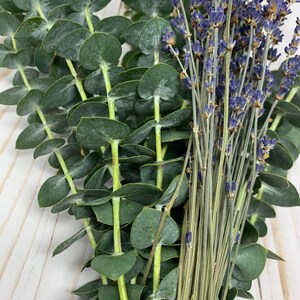 A zoomed in photo of a bunch of eucalyptus with french lavender stems in from. The bundle is on a wood-like background.