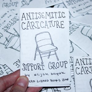 K&ouml;nnte beinhalten: Ein kleines, wei&szlig;es Zine mit dem Titel "Antisemitic Caricature" und einer handgezeichneten Stuhllustration. Der Text "Support Group" und der Name des Autors sind ebenfalls sichtbar. Andere Zines mit &auml;hnlichen Designs sind im Hintergrund.