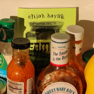 Puede incluir: Una colecci&oacute;n de productos alimenticios, que incluye botellas de salsas, aderezos y mostaza. Un libro con el texto "elijah bayuk" es visible. Una botella dice "The Sauce is the Boss". La imagen tiene una iluminaci&oacute;n c&aacute;lida y natural.