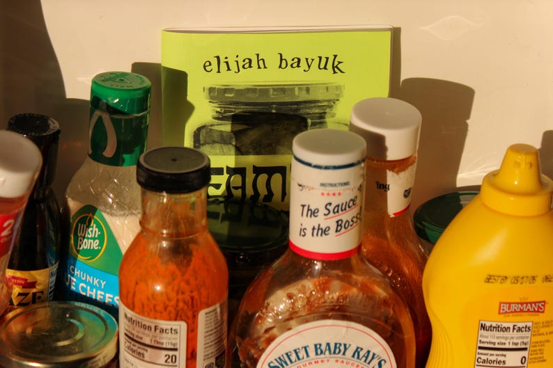 Puede incluir: Una colecci&oacute;n de productos alimenticios, que incluye botellas de salsas, aderezos y mostaza. Un libro con el texto "elijah bayuk" es visible. Una botella dice "The Sauce is the Boss". La imagen tiene una iluminaci&oacute;n c&aacute;lida y natural.