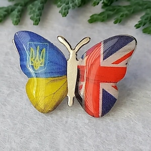 May include: A metal butterfly pin with the Ukrainian flag on one wing and the Union Jack on the other wing.