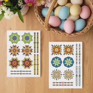 Peut inclure: Deux feuilles de tatouages temporaires colorés avec des motifs d'étoiles et de fleurs. Un panier d'œufs de Pâques aux couleurs pastel est à proximité, ainsi qu'un vase de fleurs. Les tatouages présentent des teintes vertes, oranges, jaunes et violettes.