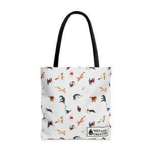 K&ouml;nnte beinhalten: Wei&szlig;e Tragetasche mit einem sich wiederholenden Muster von verspielten Hunden in verschiedenen Posen, einige mit Frisbees. Die Tasche hat schwarze Griffe und ein kleines Logo mit der Aufschrift "WET LAB CREATIVE".