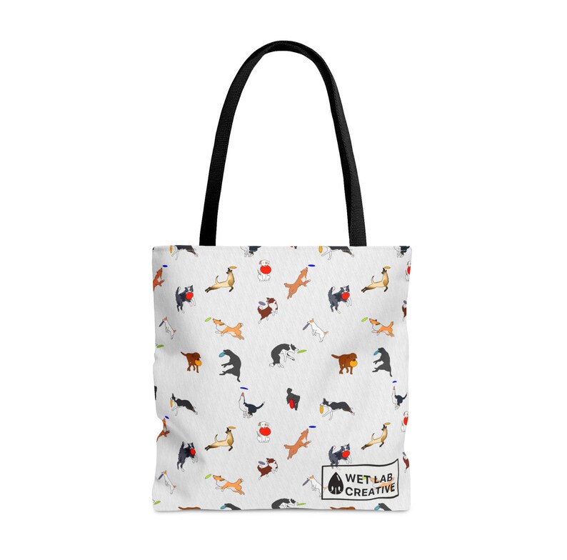 K&ouml;nnte beinhalten: Wei&szlig;e Tragetasche mit einem sich wiederholenden Muster von verspielten Hunden in verschiedenen Posen, einige mit Frisbees. Die Tasche hat schwarze Griffe und ein kleines Logo mit der Aufschrift "WET LAB CREATIVE".