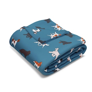Può includere: Una coperta piegata color verde acqua con un motivo ripetuto di cani bianchi, marroni e neri. La coperta è morbida e accogliente, perfetta per rannicchiarsi sul divano o sul letto. I cani sono in pose diverse.