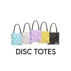 K&ouml;nnte beinhalten: F&uuml;nf Tragetaschen mit schwarzen Griffen, jede mit einem anderen Muster zum Thema Hunde. Die Taschen sind in verschiedenen Farben erh&auml;ltlich: Hellblau, Wei&szlig;, Lavendel, Gelb und Schwarz. Der Text "DISC TOTES" ist in gro&szlig;en, schwarzen Buchstaben darunter zu sehen.