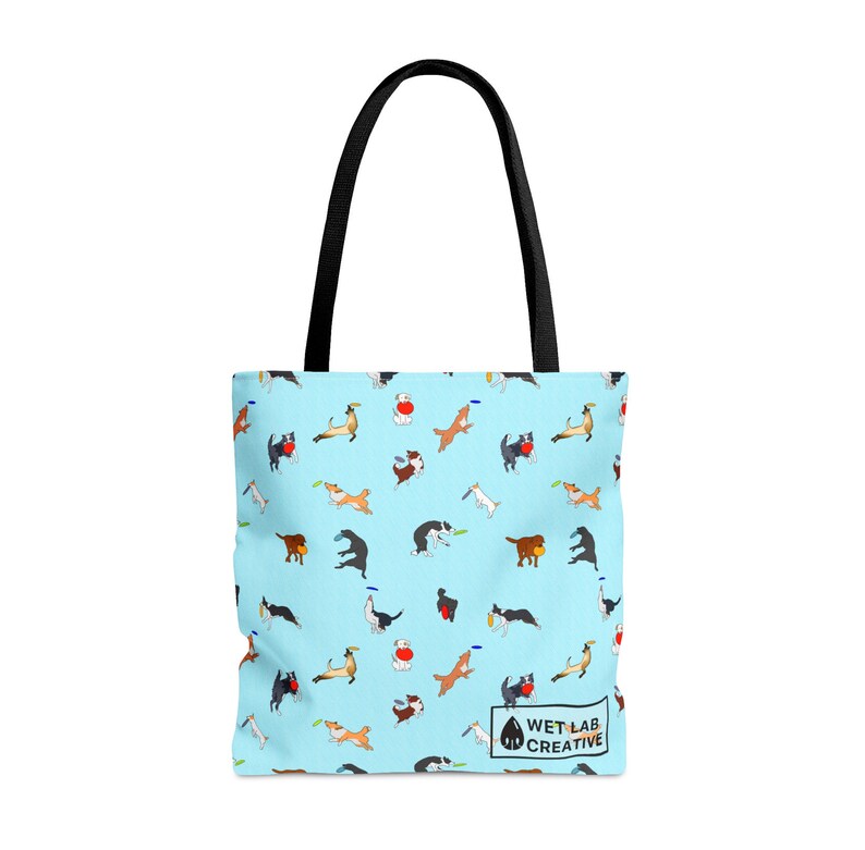 K&ouml;nnte beinhalten: Hellblaue Tragetasche mit einem sich wiederholenden Muster von spielenden Hunden. Die Tasche hat schwarze Griffe und den Text "WET LAB CREATIVE". Die Hunde sind in verschiedenen Posen, einige fangen Frisbees.