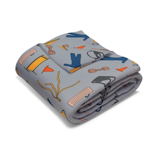 May include: A folded gray blanket with a repeating pattern of fitness and sports-related illustrations. The design includes orange traffic cones, blue athletic wear, dumbbells, and other sports equipment. The blanket is folded and appears soft.