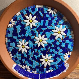 May include: A terracotta planter with a mosaic design featuring blue and turquoise tiles and white daisy flowers.