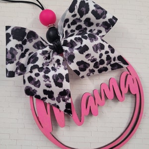 May include: Pink wooden circle with the word "Mama" written in white. A black and white leopard print bow is attached to the top of the circle.