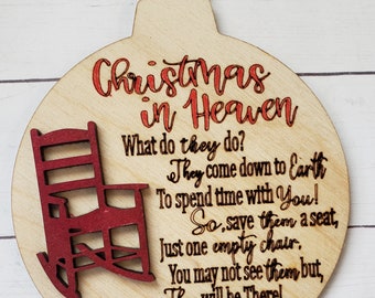 May include: A wooden Christmas ornament shaped like a circle with a rocking chair cutout. The ornament is painted in shades of brown and red. The text on the ornament reads "Christmas in Heaven. What do they do? They come down to Earth To spend time with You! So, save them a seat, Just one empty chair. You may not see them but, They will be There!"