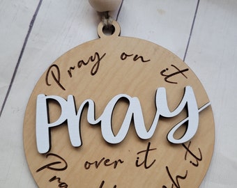 May include: A wooden ornament with the words "Pray on it, Pray over it, Pray through it" engraved on it. The ornament is hanging from a string with wooden beads.