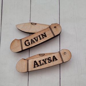 May include: Two wooden pocket knife shaped ornaments with the names "Gavin" and "Alyssa" engraved on them.