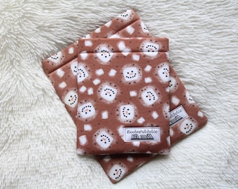 May include: Two brown fabric pouches with a repeating pattern of white snowmen and white square accents. The pouches are stacked on top of each other. Each pouch has a small white label with the text "Booknördcheldie".