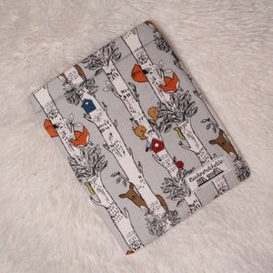 May include: A gray fabric book sleeve with a white and black pattern of trees, birds, and animals. The text "Booknookliebe" is printed on the sleeve.