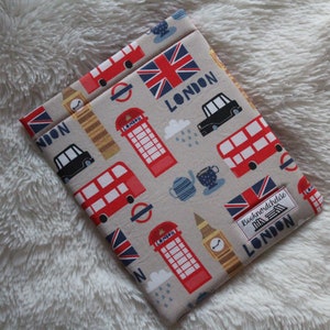 Puede incluir: Una cubierta de libro beige con temática de Londres. La cubierta presenta autobuses rojos de dos pisos, taxis negros, cabinas telefónicas rojas, el Big Ben y la bandera de la Union Jack. El texto "Booknordchidae LONDON" está impreso en la cubierta.