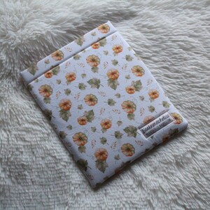 May include: A white book cover with a pumpkin and leaf pattern. The cover has a small label that says "Buchmacherei" with a website address.
