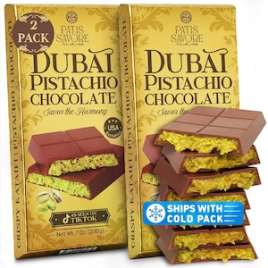 May include: Two gold-toned boxes of Patis Savore Dubai Pistachio Chocolate, each labeled 7 Oz (200g). The packaging features text including 'Savor the Harmony' and 'As Seen on TikTok'. A stack of chocolate bars shows a green pistachio filling.
