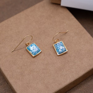 Puede incluir: Un par de pendientes colgantes de oro con piedras rectangulares de mosaico azul y plata.
