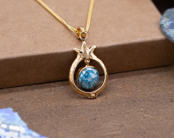 Peut inclure: Un collier en or avec un pendentif en forme de grenade bleu et or. Le pendentif est en métal martelé et présente une pierre ronde bleue au centre.