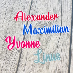 Könnte beinhalten: Vier gestickte Bügelbilder mit verschiedenen Namen. Die Namen sind Alexander in Rot, Maximilian in Blau, Yvonne in Pink und Linus in Hellblau.