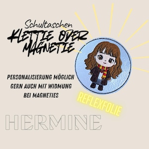 Könnte beinhalten: Ein runder, hellblauer Hermione-Aufnäher mit einem Cartoon-Bild von Hermine Granger. Der Aufnäher ist von deutschem Text umgeben, darunter "Klettie oder Magnetie" und "Hermine". Das Wort "REFLEXFOLIE" ist gelb.