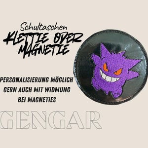 Könnte beinhalten: Ein runder schwarzer Aufnäher mit einer Stickerei des violetten Gengar-Charakters mit orangen Augen und weißem Grinsen. Der Text lautet: Schultaschen KLETTIE ODER MAGNETIE, PERSONALISIERUNG MÖGLICH GERN AUCH MIT WIDMUNG BEI MAGNETIES, und GENGAR.
