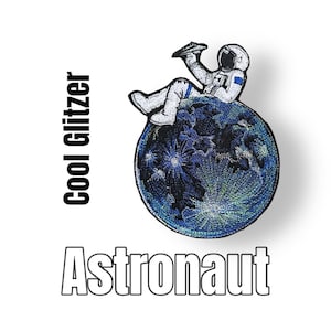 Könnte beinhalten: Gestickter Aufnäher eines Astronauten, der auf einem blauen und grünen Planeten sitzt, mit den Worten "Cool Glitzer" und "Astronaut" darunter.