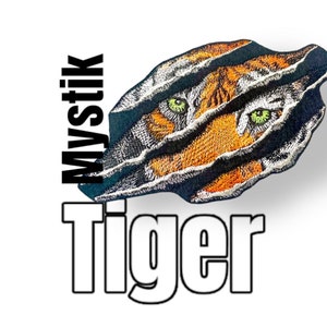 Könnte beinhalten: Ein schwarzes und orangefarbenes Tigergesicht, das aus einem zerrissenen schwarzen Stoff mit den Worten "Mystik Tiger" in weißer Schrift hervorlugt.