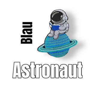 Könnte beinhalten: Ein gestickter Aufnäher mit einem Astronauten, der ein Buch liest, während er auf einem blauen Planeten mit einem Ring sitzt. Der Text "Blau Astronaut" befindet sich unter dem Bild.