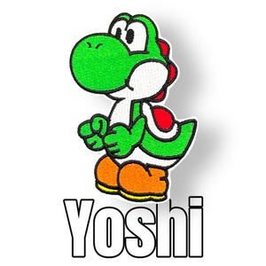 Könnte beinhalten: Gestickter Aufnäher mit Yoshi, einem grünen, dinosaurierartigen Charakter mit weißem Bauch, roten Schalenakzenten und orangefarbenen Schuhen. Das Wort "Yoshi" wird darunter in fetter, umrandeter Schrift angezeigt.