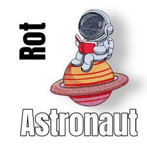 Könnte beinhalten: Ein gestickter Aufnäher mit einem Astronauten, der auf einem Planeten mit Ringen sitzt und ein Buch liest. Der Astronaut trägt einen weißen Raumanzug mit einem schwarzen Helm und ein rotes Buch. Der Planet ist gelb mit roten Streifen und einem rosafarbenen Ring. Der Text "Rot" ist in Schwarz über dem Astronauten und "Astronaut" ist in Weiß unter dem Planeten.